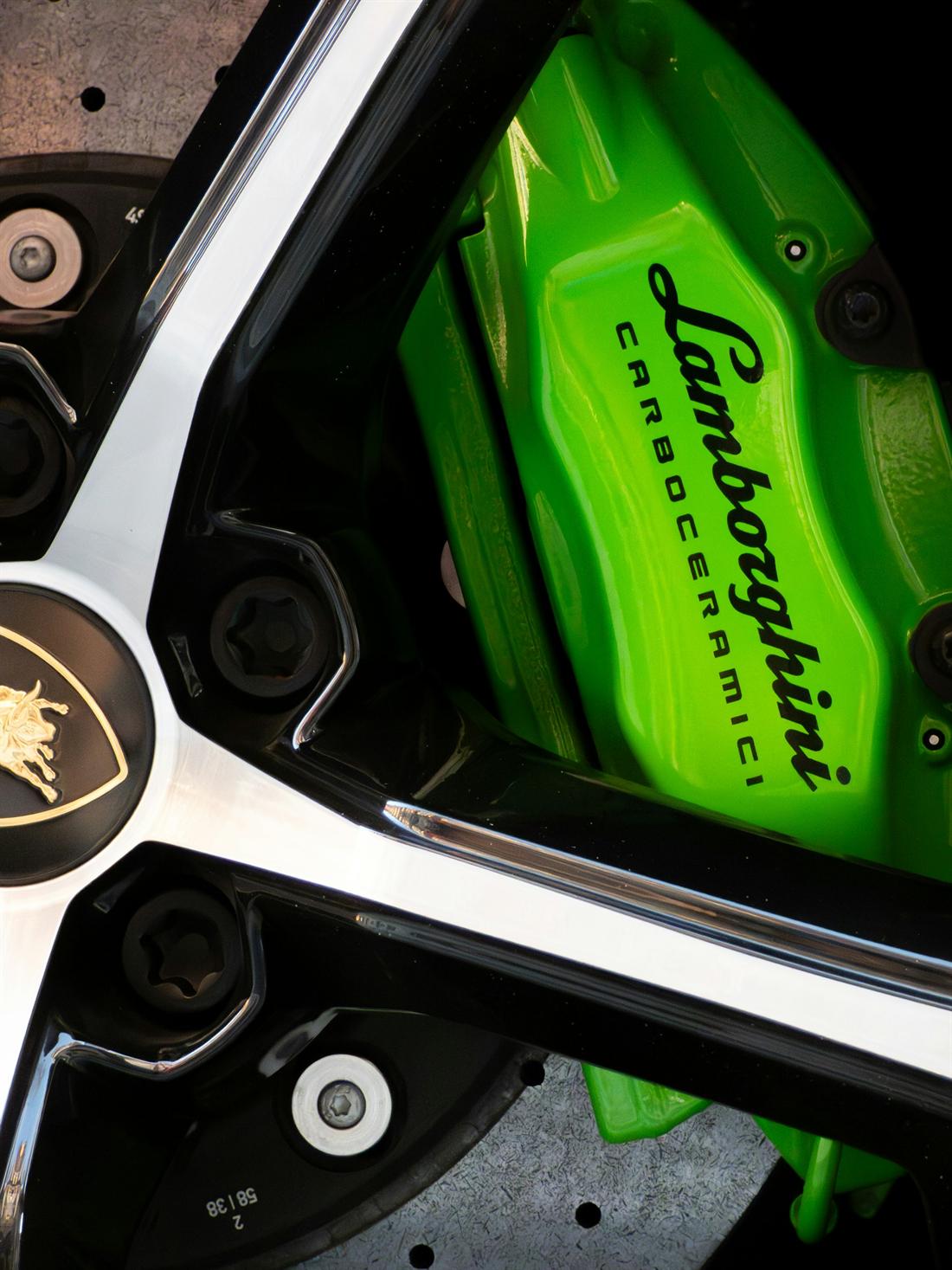 Close-up of a green carbon-ceramic brake caliper behind a polished wheel spoke