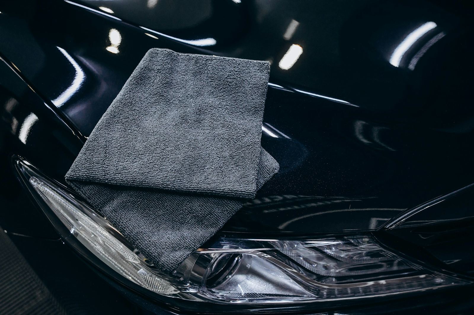 Deep gloss black paint after correction, with crisp reflections and a microfibre towel resting beside the headlight
