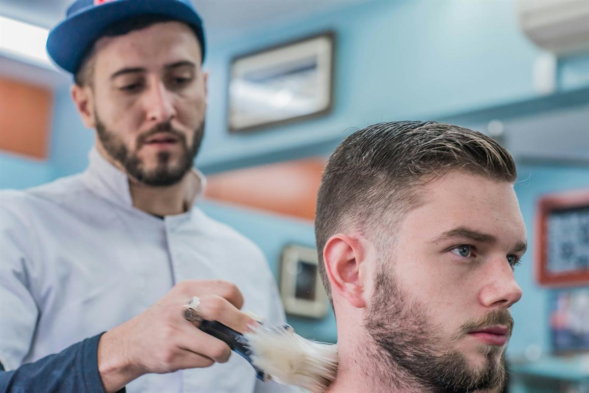 A barber brushing the neck of a bearded client after a haircut