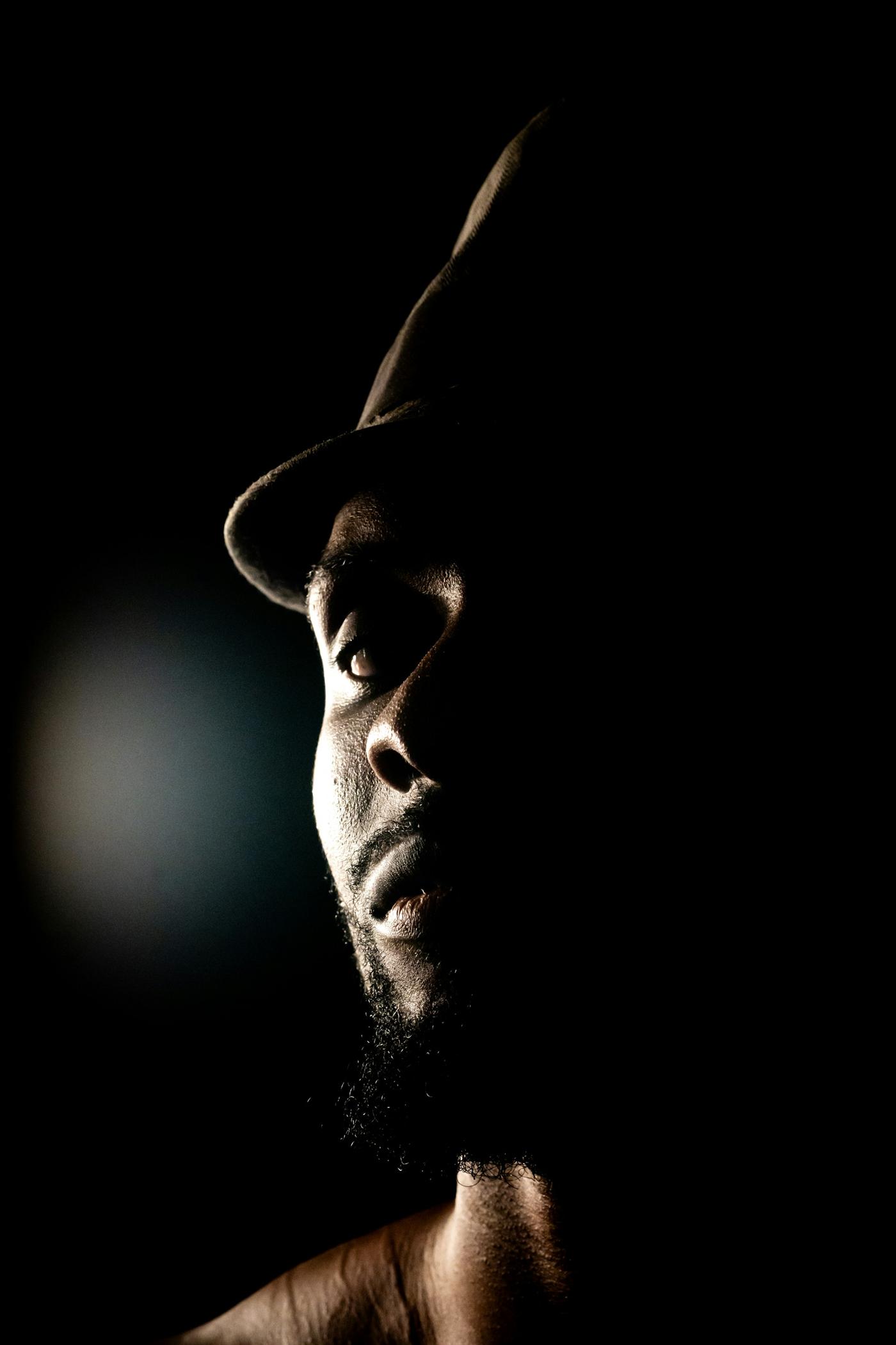 Dramatic low-key portrait of a man in a hat, lit from one side against a black background
