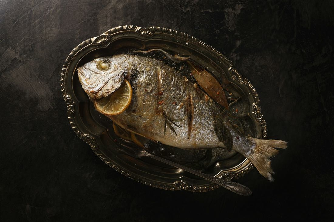 Whole grilled sea bass with lemon on an antique silver platter