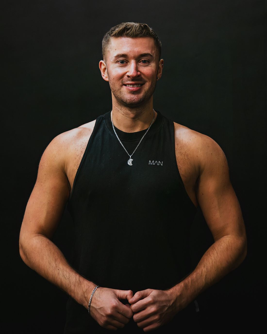Portrait of Dean Kruger, head of conditioning, smiling with hands clasped in front of a dark backdrop