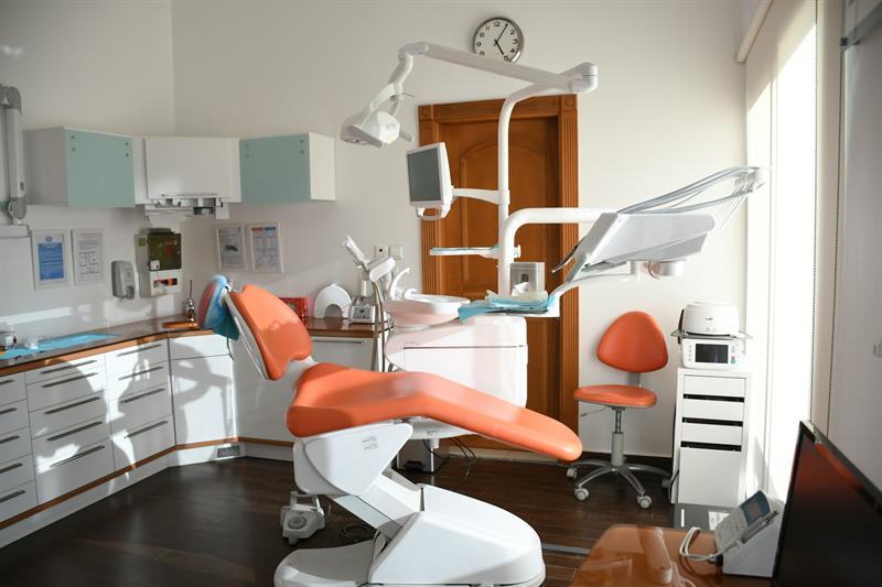 A sunlit surgery with an orange dental chair and pale timber door
