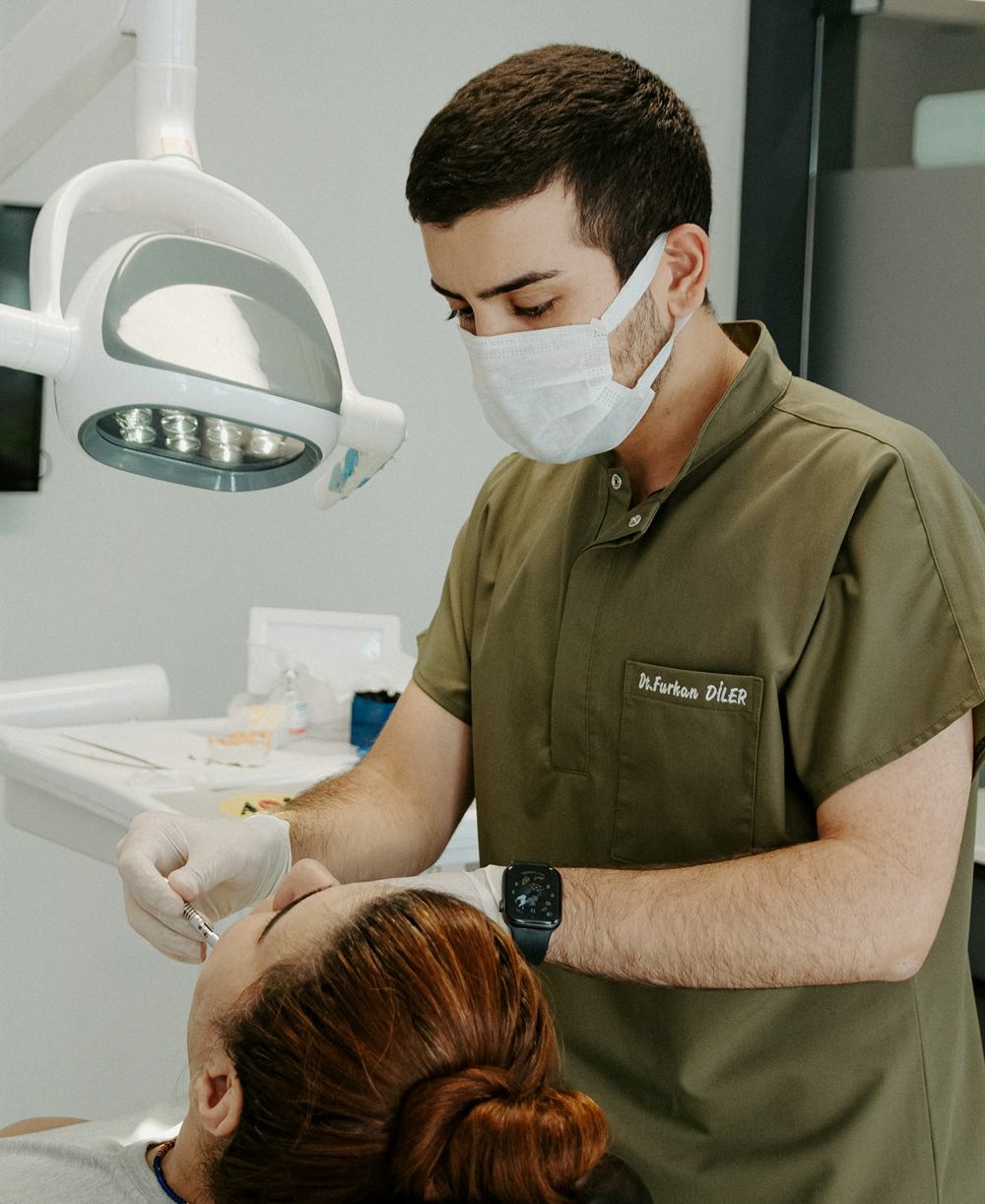 A dentist in a green scrub top and mask examining a patient lying back in the chair