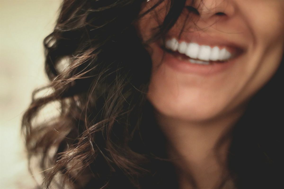 Close-up of a woman’s bright smile as she laughs, hair falling across her face